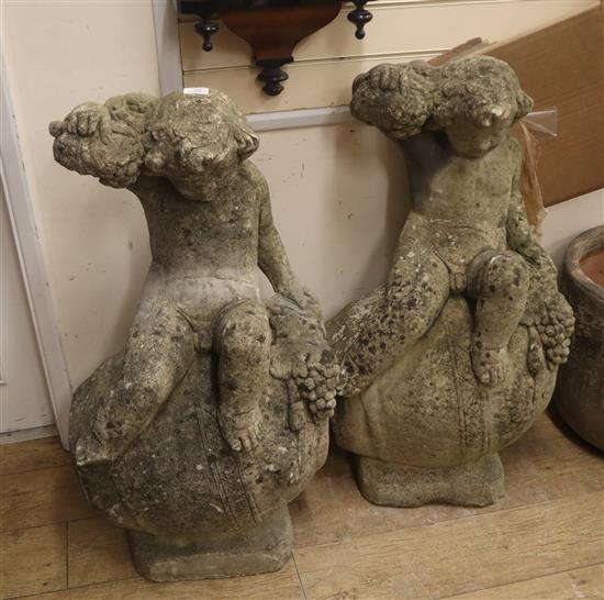 A pair of reconstituted stone Bacchanalian cherubs sitting on wine barrels (a.f.) H.94cm